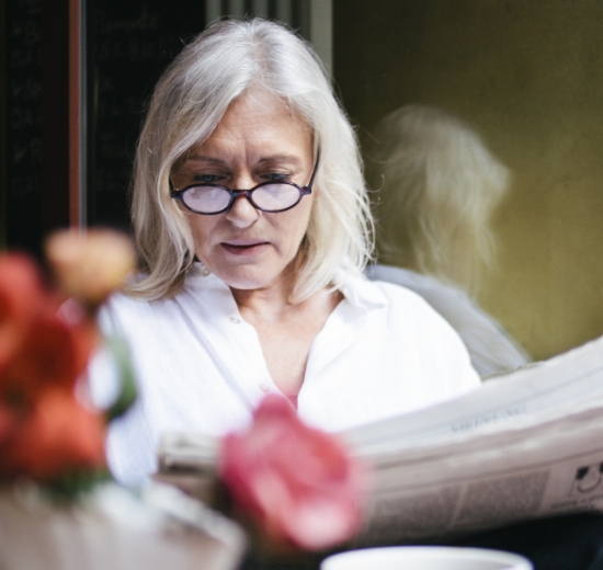 Ältere Dame mit Brille liest Zeitung.
